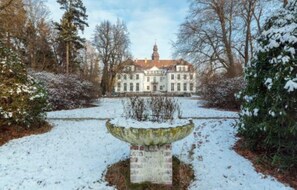 A large, historic building with a symmetrical facade, a central tower, and a snow-covered garden with a stone fountain. - Holiday Home in Ortrand With Garden (Ortrand)