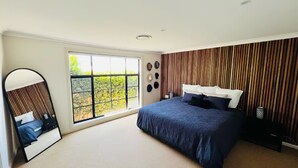 Un dormitorio moderno con una cama grande, una ventana con vistas, un espejo y una pared de madera decorativa.