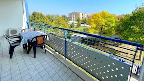 A balcony with a table and chairs, a view of buildings and trees, and a blue railing. - Apartment in Caorle Near Adriatic Sea (Caorle)