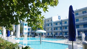 A swimming pool with lounge chairs and umbrellas, surrounded by buildings with balconies. - Apartment in Caorle Near Adriatic Sea (Caorle)