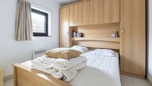 Una camera da letto con un letto, un armadio, una finestra con tende e un termosifone.