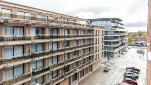 Un hotel a più piani con balconi, un parcheggio e un edificio moderno sullo sfondo.