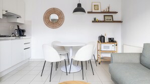 Una cucina moderna con mobili bianchi, uno specchio rotondo, un tavolo da pranzo con sedie, una lampada a sospensione e un forno a microonde su uno scaffale.
