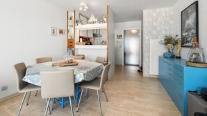 A dining area with a table set for four, a kitchen in the background, and a blue cabinet with decorative items.