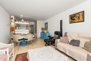 A living room with a sofa, a dining table with chairs, a massage chair, and a bookshelf. - 2 bedroom accommodation in Nieuwpoort (Nieuwpoort)