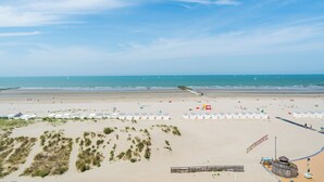 A beach with white beach huts, a sandy area with sparse vegetation, and a wooden structure.