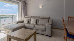 A modern living room with a sofa, a wooden coffee table, and a dining table with chairs. - 2 bedroom accommodation in Nieuwpoort (Nieuwpoort)