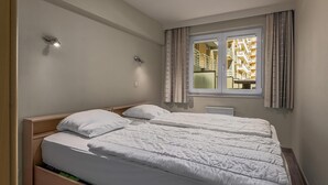 A double bed with white bedding, a bedside table, and a window with curtains. - 2 bedroom accommodation in Nieuwpoort (Nieuwpoort)