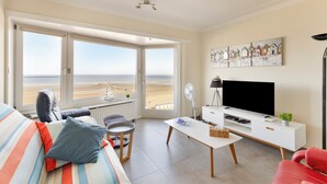 Una sala de estar con sofá, una mesa de centro, televisor y un gran ventanal con vista a la playa.