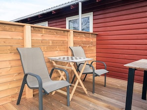 A wooden deck with two chairs and a small table, adjacent to a red building with windows. - 4 Star Holiday Home in Jerup (Jerup)
