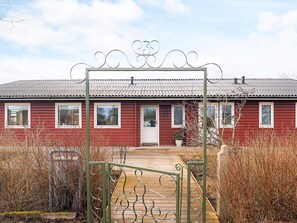 Una casa in legno rossa con un cancello in metallo e un vialetto in legno che conduce all'ingresso.