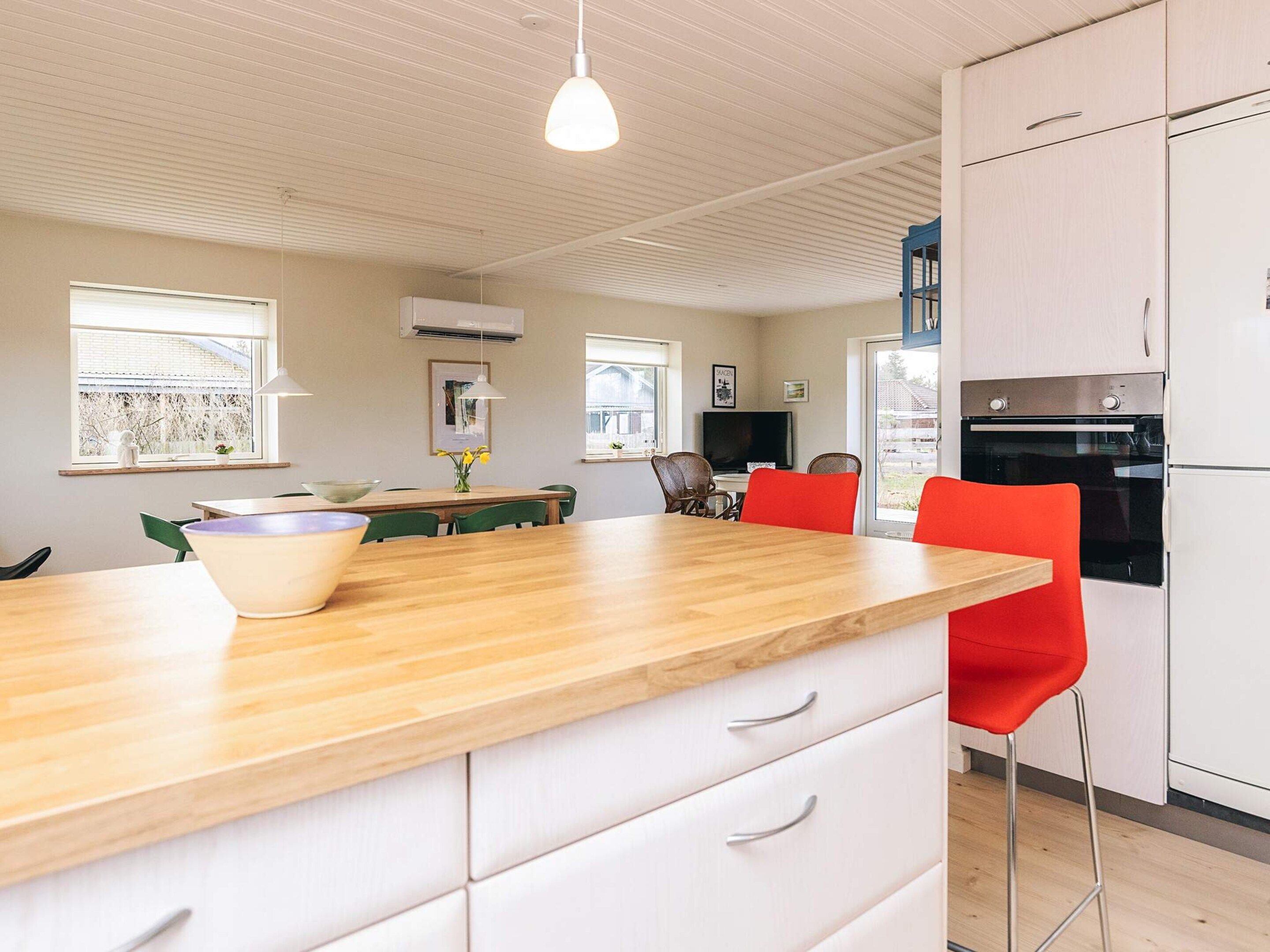 A modern kitchen with white cabinets, a wooden countertop, and red chairs.