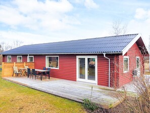 Une maison en bois rouge avec un patio couvert, une porte-fenêtre coulissante et un toit en métal.