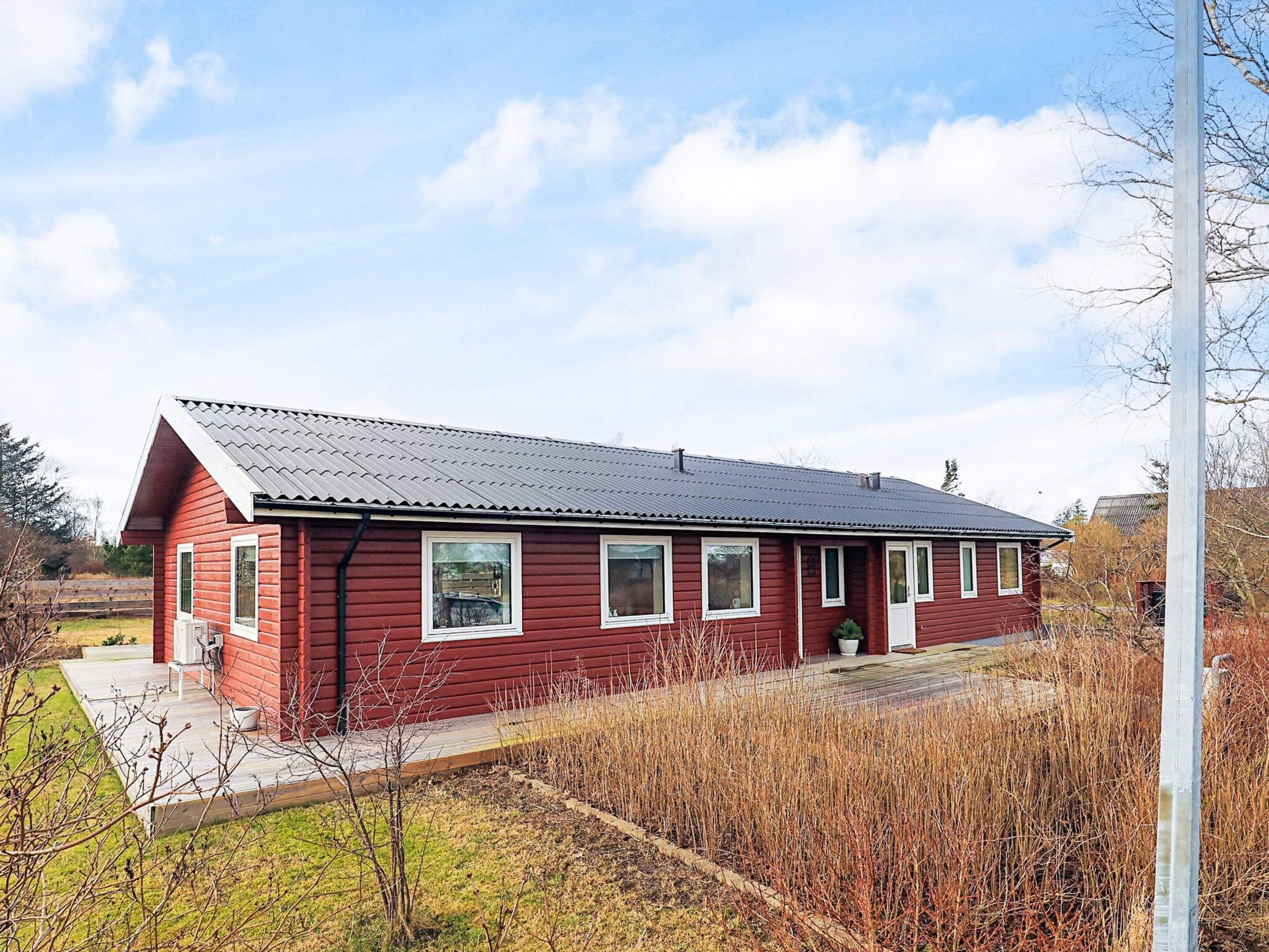 A red wooden house with a sloped roof, a front porch, and a small garden area.