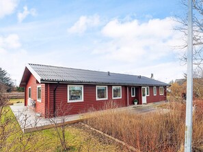 A red wooden house with a sloped roof, a front porch, and a small garden area. - 4 Star Holiday Home in Jerup (Jerup)