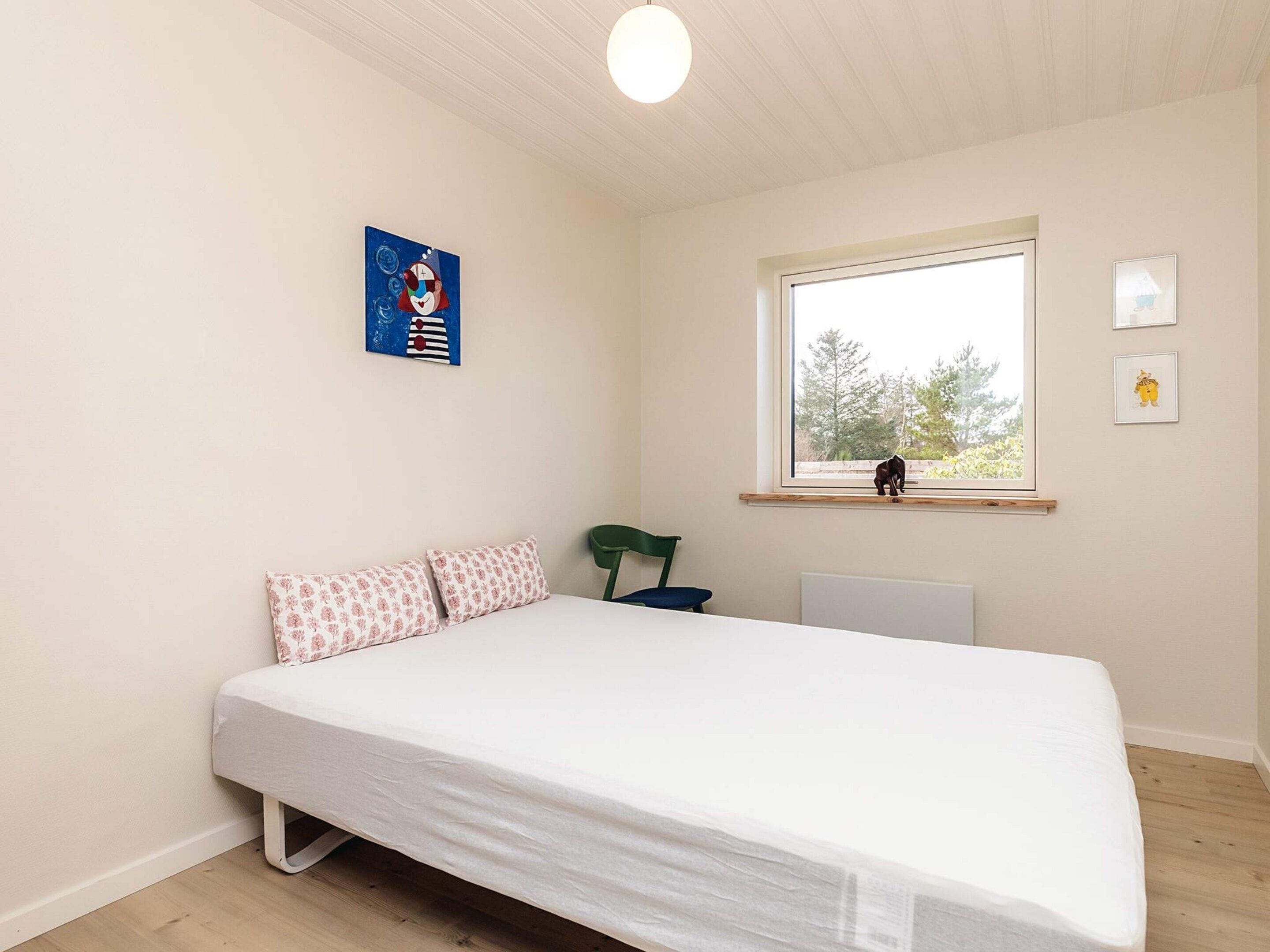 A bedroom with a bed, a window, a radiator, and a wall with a picture.