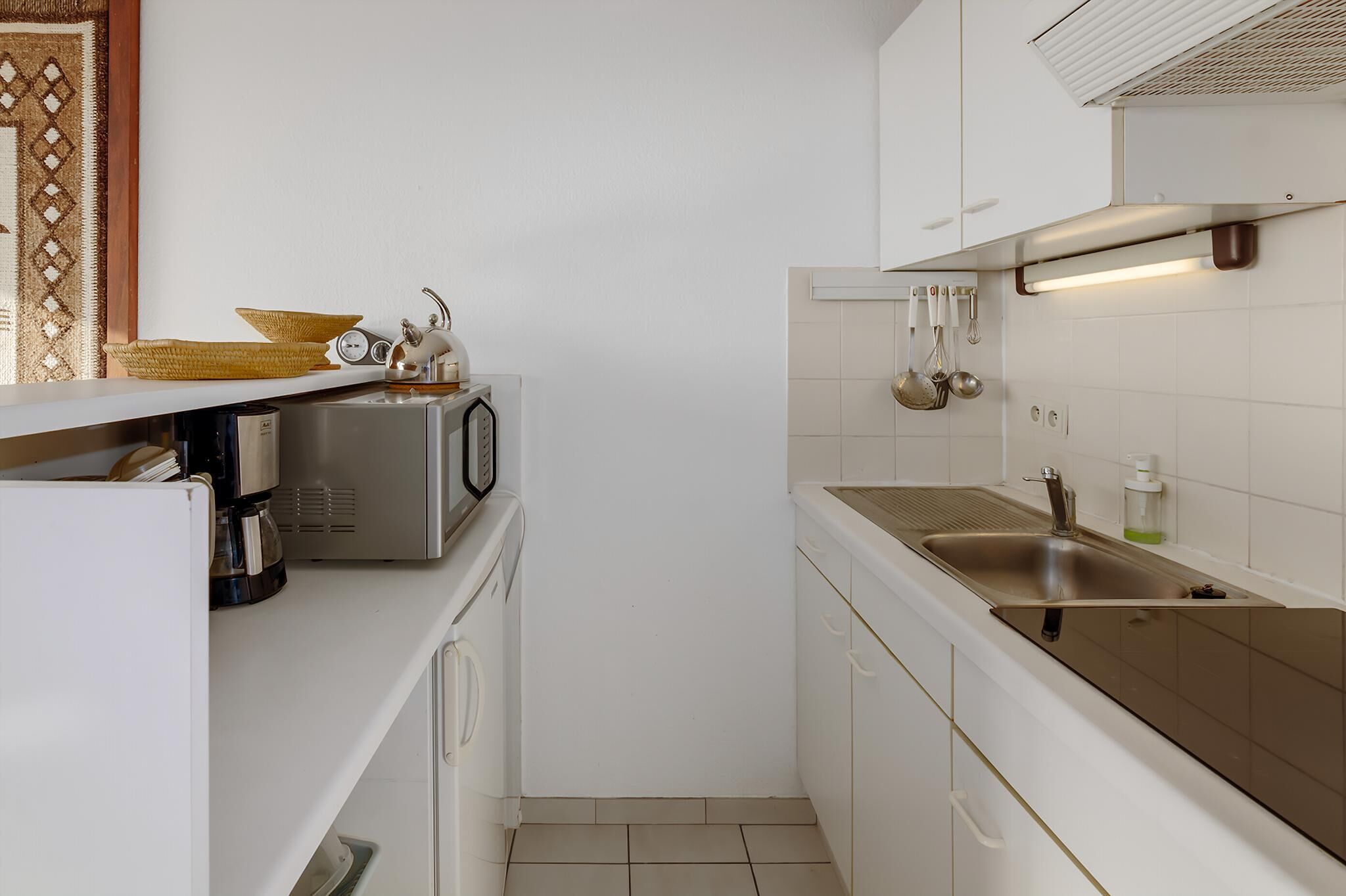 Una cocina compacta equipada con microondas, cafetera y un lavamanos con utensilios colgando.