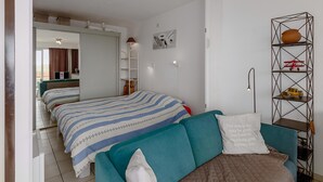 A hotel room with two beds, a teal sofa, a bookshelf, and a wall-mounted shelf with decorative items. - 1 bedroom accommodation in NIEUWPOORT (NIEUWPOORT)