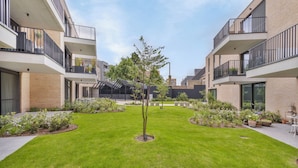 Une cour intérieure avec un arbre au centre, entourée d’une pelouse bien entretenue et de plantes en pot.