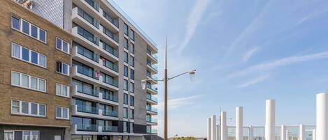 Un edificio moderno de varios pisos con fachadas de ladrillo y vidrio, mesas al aire libre y cielo despejado.