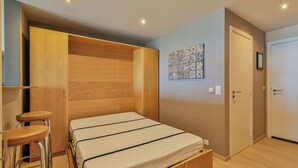 Une chambre à coucher comprenant un lit, une armoire en bois, un tabouret et une œuvre d’art accrochée au mur.