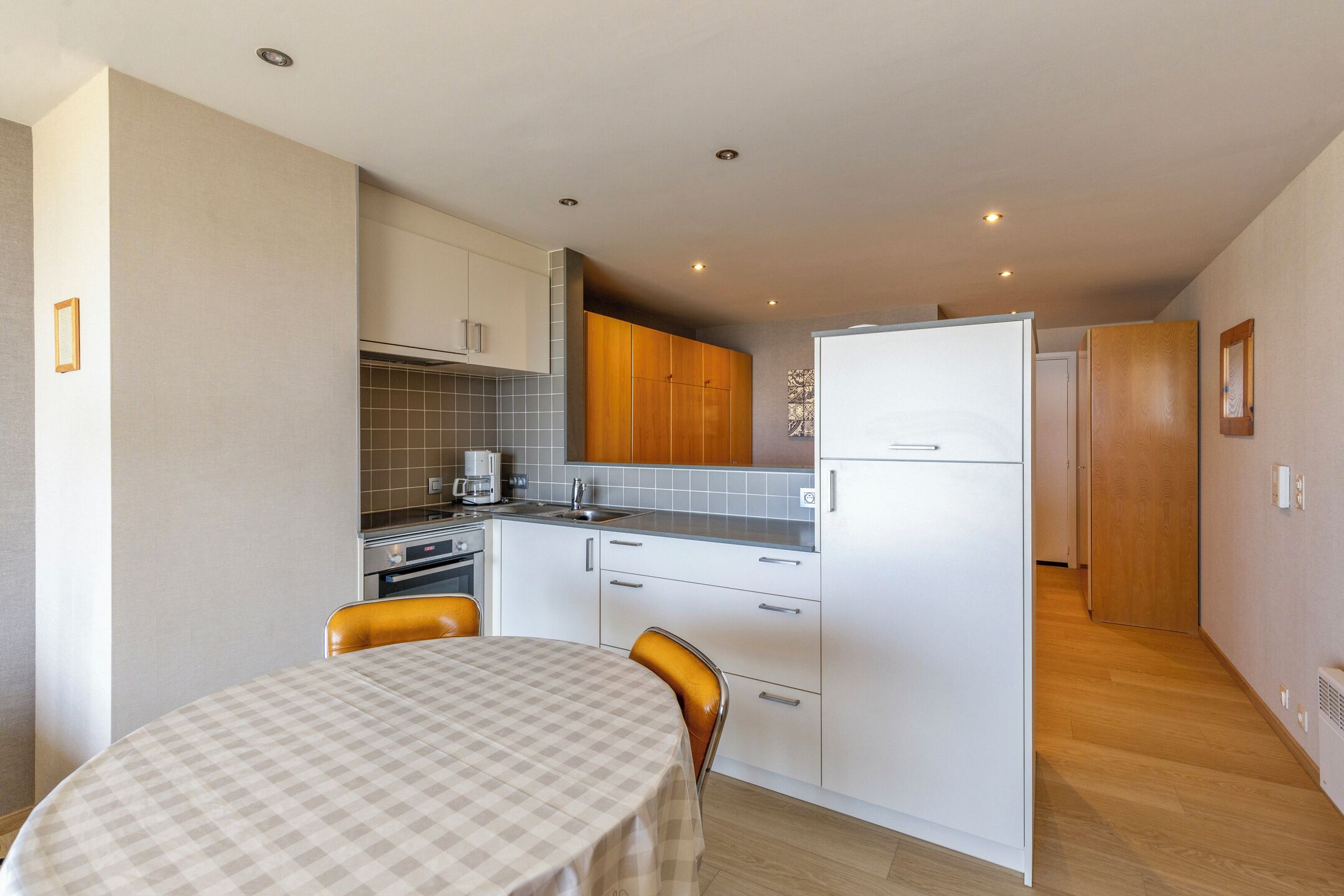 Cocina compacta con mesa de comedor, armarios blancos y un refrigerador.