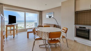 Une cuisine moderne dotée d’une grande fenêtre, un coin repas avec une table et des chaises, et un téléviseur à écran plat posé sur un meuble.