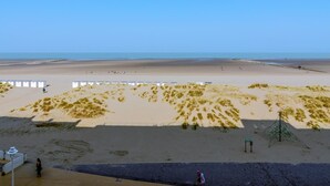 Ein Strand mit blauem Himmel, sandigen Dünen und einigen Spaziergängern.