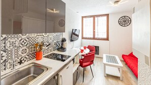 A compact kitchen with a sink, stove, and a dining area with a red chair and table. - Modern and cozy studio at the chairlift's base (Saint-François-Longchamp)