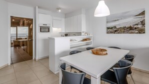 A modern kitchen with white cabinets, a central island, and a dining area with a white table and black chairs.
