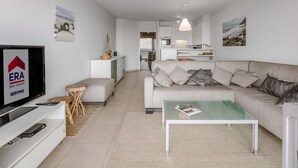 A modern living room with a sofa, coffee table, and TV. There is a kitchen in the background.