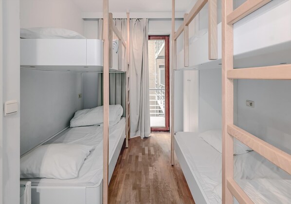 Un couloir étroit, avec des lits superposés de chaque côté, qui mène à une porte donnant sur l’extérieur.