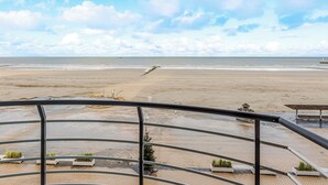 A beach view from a balcony with metal railings, a sandy beach, and a calm sea.