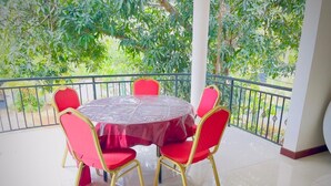 A round table with a transparent cover and red chairs, set on a balcony with a railing and greenery in the background. - Cinnamon Tree (Anuradhapura)