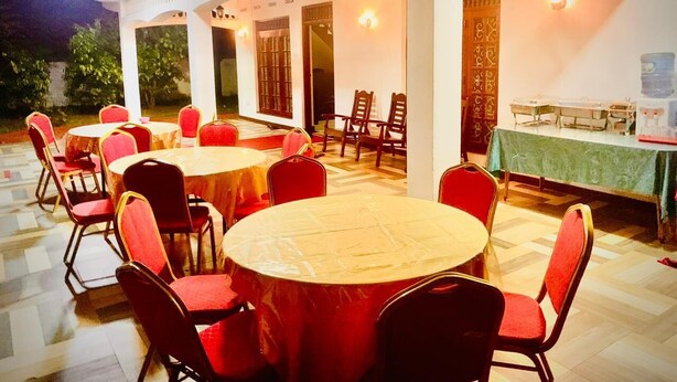 A dining area with round tables and red chairs, a water dispenser, and a green tablecloth. - Cinnamon Tree (Anuradhapura)