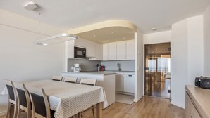 A modern kitchen with white cabinets, a microwave, and a coffee maker. There is a dining area with a table and chairs. - 2 bedroom accommodation in Nieuwpoort (Nieuwpoort)