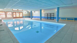 Piscina interior com água azul cristalina, paredes azulejadas e teto com padrão de grade.