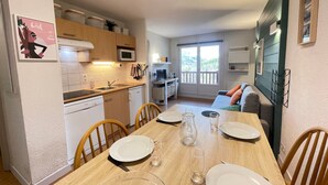 Cozinha compacta com área de jantar, sofá e varanda com vista.