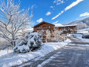 Eine Holzhütte mit Balkon, umgeben von schneebedeckten Bäumen und einem klaren Himmel.