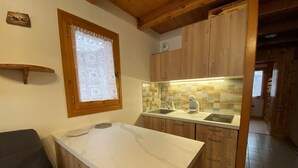 A kitchen with wooden cabinets, a marble countertop, and a window with lace curtains. - Central 1-bedroom apartment, well equipped with WIFI (Crest-Voland)