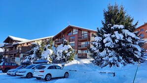 A hotel with multiple floors, balconies, and a parking area with several cars. - Central 1-bedroom apartment, well equipped with WIFI (Crest-Voland)