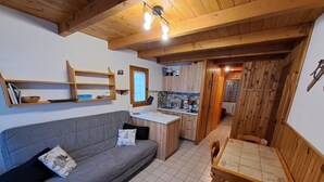 A cozy living room with a grey sofa, wooden dining table, and a kitchen area with wooden cabinets and a window. - Central 1-bedroom apartment, well equipped with WIFI (Crest-Voland)