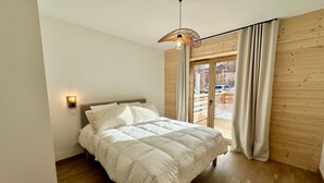 Ein Schlafzimmer mit einem Bett, Holzwänden, einer Deckenleuchte und Blick durch eine Glastür.