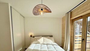 Ein Schlafzimmer mit einem großen Bett, einer Wandleuchte und Blick ins Freie durch eine Schiebetür.