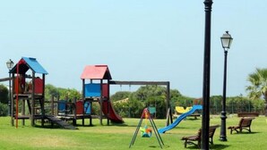 A playground with various play structures including slides and climbing areas, surrounded by a grassy field and a street lamp. - Beachfront Apartments with Pool in Atlanterra, Zahara de los Atunes (Zahara de los Atunes)