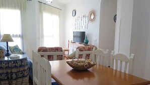 A dining area with a wooden table, blue upholstered chairs, a decorative bowl, and a television in the background. - Beachfront Apartments with Pool in Atlanterra, Zahara de los Atunes (Zahara de los Atunes)