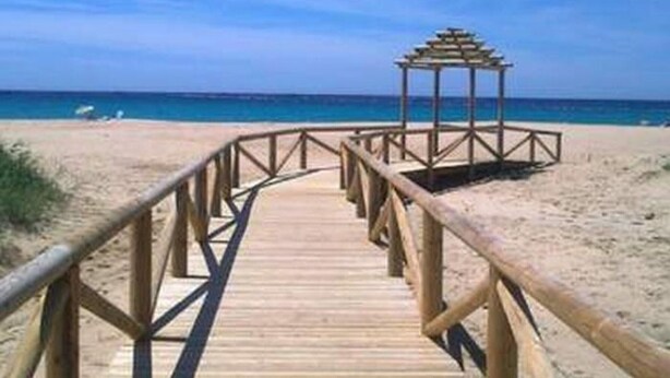 Un muelle de madera que conduce a una playa con una estructura tipo quiosco.