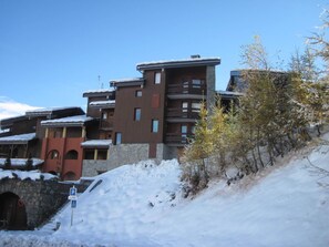 A multi-story building with a stone facade and wooden balconies, surrounded by snow-covered ground and trees.