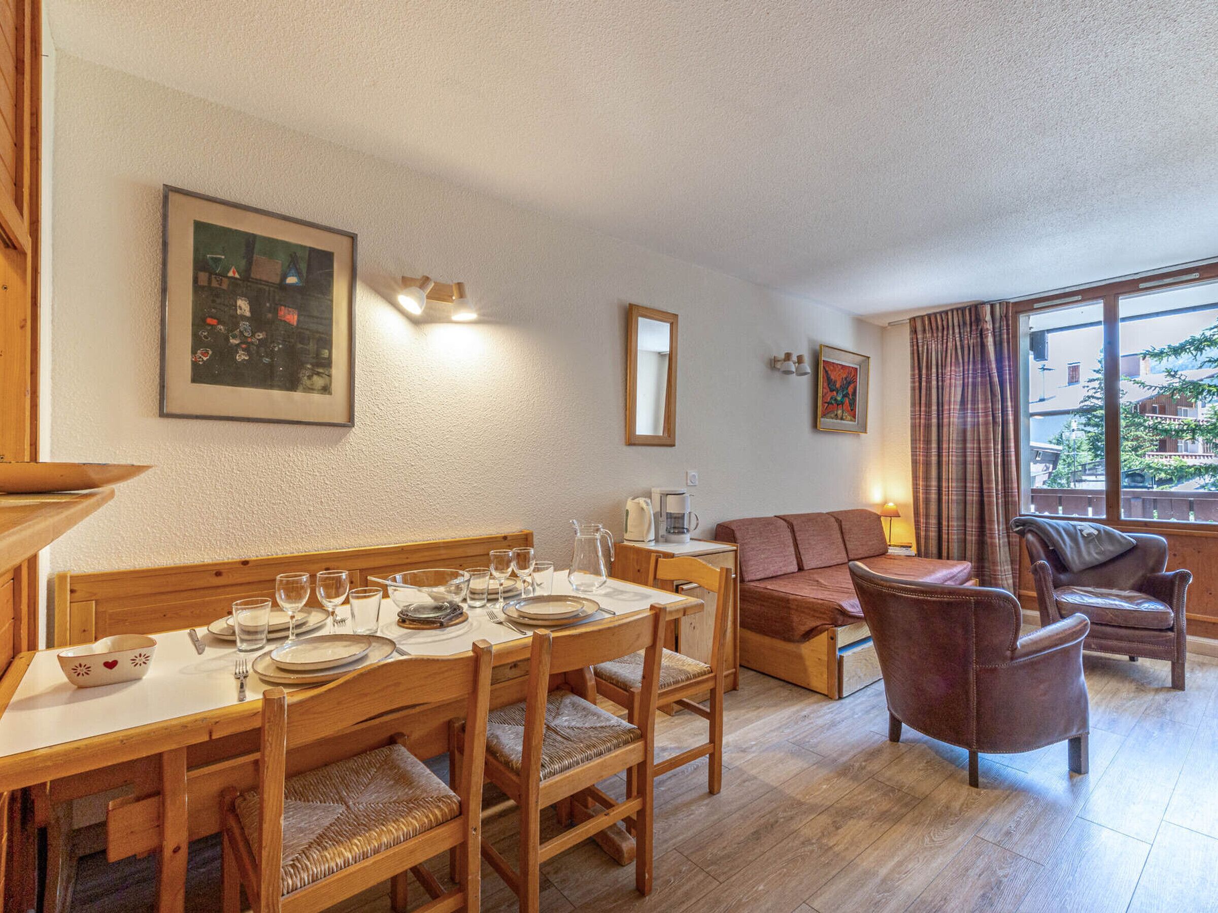 Un coin repas avec une table en bois dressée pour quatre personnes, un canapé et deux fauteuils.
