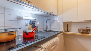 Une cuisine avec des meubles blancs, un plan de travail noir, une casserole rouge, un évier et un égouttoir à vaisselle.